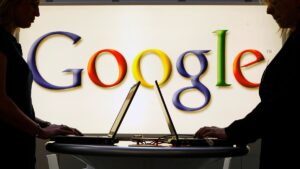 Exhibitors work on laptop computers in front of an illuminated sign of the Google logo at the industrial fair Hannover Messe in Hanover, Germany in 2014