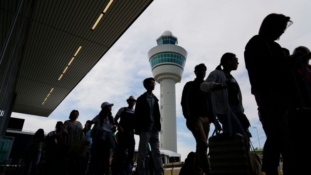 Travelers wait in line outside the terminal building to check in and board flights at Amsterdam