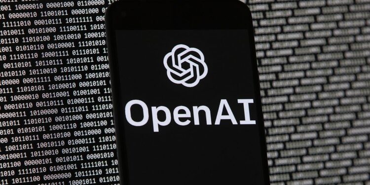 OpenAI lancia il suo assistente vocale AI dopo un ritardo dovuto a problemi di sicurezza 35 The OpenAI logo appears on a mobile phone in front of a computer screen with random binary data.