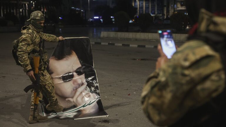 A Syrian opposition fighter takes a picture of a comrade stepping on a portrait of Syrian President Bashar Assad in Aleppo, 30 November, 2024