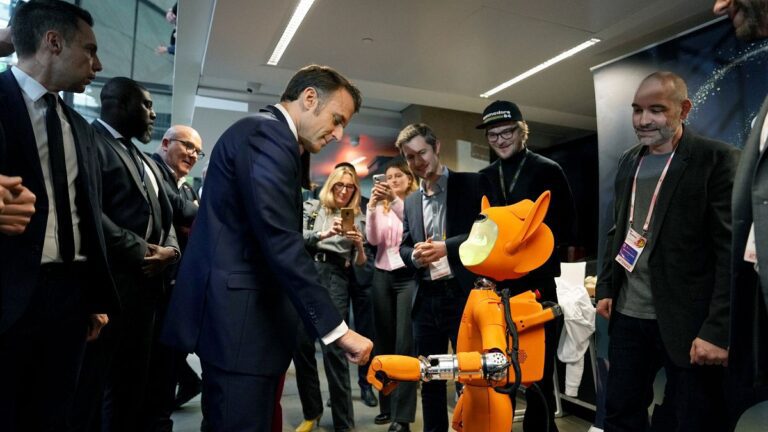 French President Emmanuel Macron, center left, bumps fists with a robot during a visit to Station F, as part of an event on the sidelines of the Artificial Intelligence Action