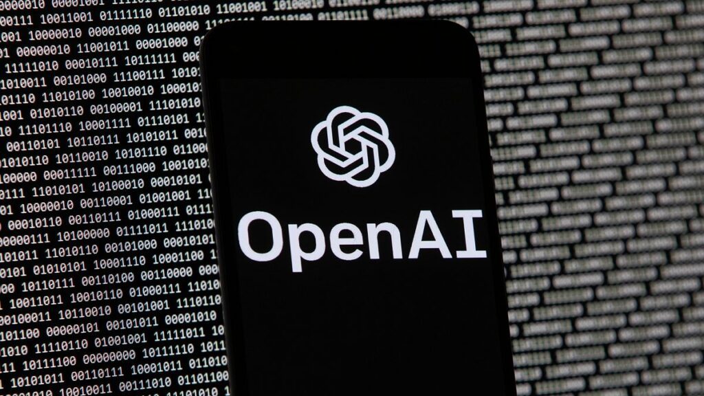 The OpenAI logo appears on a mobile phone in front of a computer screen with random binary data, March 9, 2023, in Boston.
