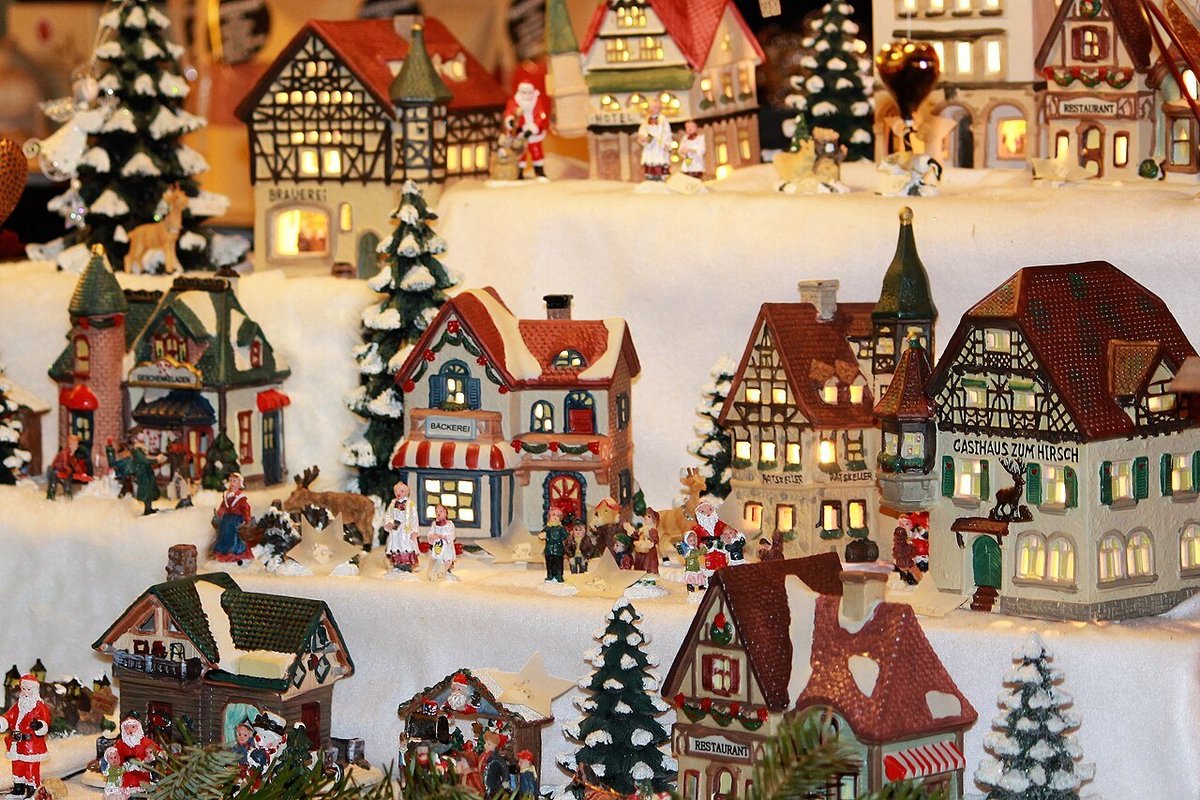 Casette natalizie in miniatura illuminate e alberelli innevati esposti a una bancarella dei mercatini di Natale di Bolzano