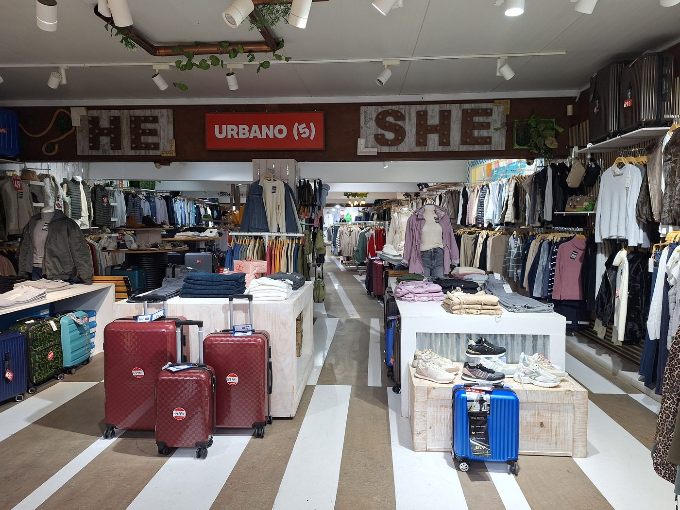 Interno di un negozio di abbigliamento con giacche, maglieria e jeans appesi e piegati sui banchi espositivi