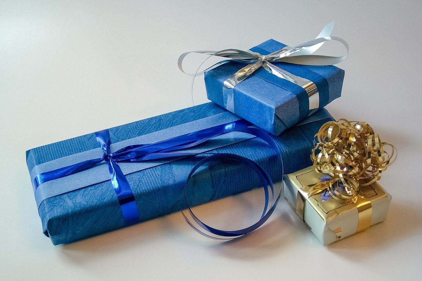Tre pacchetti regalo incartati con carta blu e argento e chiusi con nastri e fiocchi su un fondo chiaro