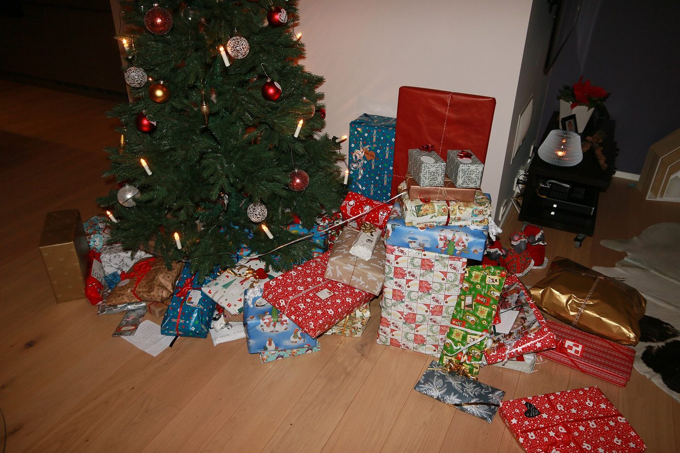 Numerosi pacchi regalo incartati con carte natalizie colorate ai piedi di un albero di Natale addobbato con luci e palline