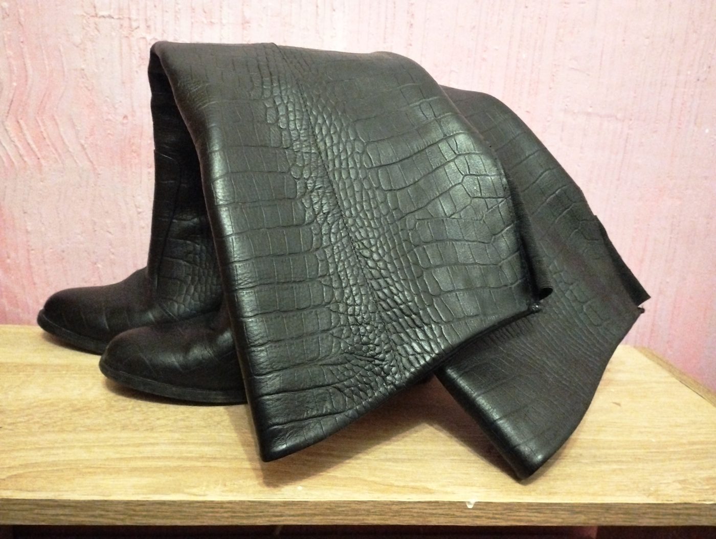 Paio di stivali alti da donna in pelle nera stampata cocco appoggiati su un ripiano di legno