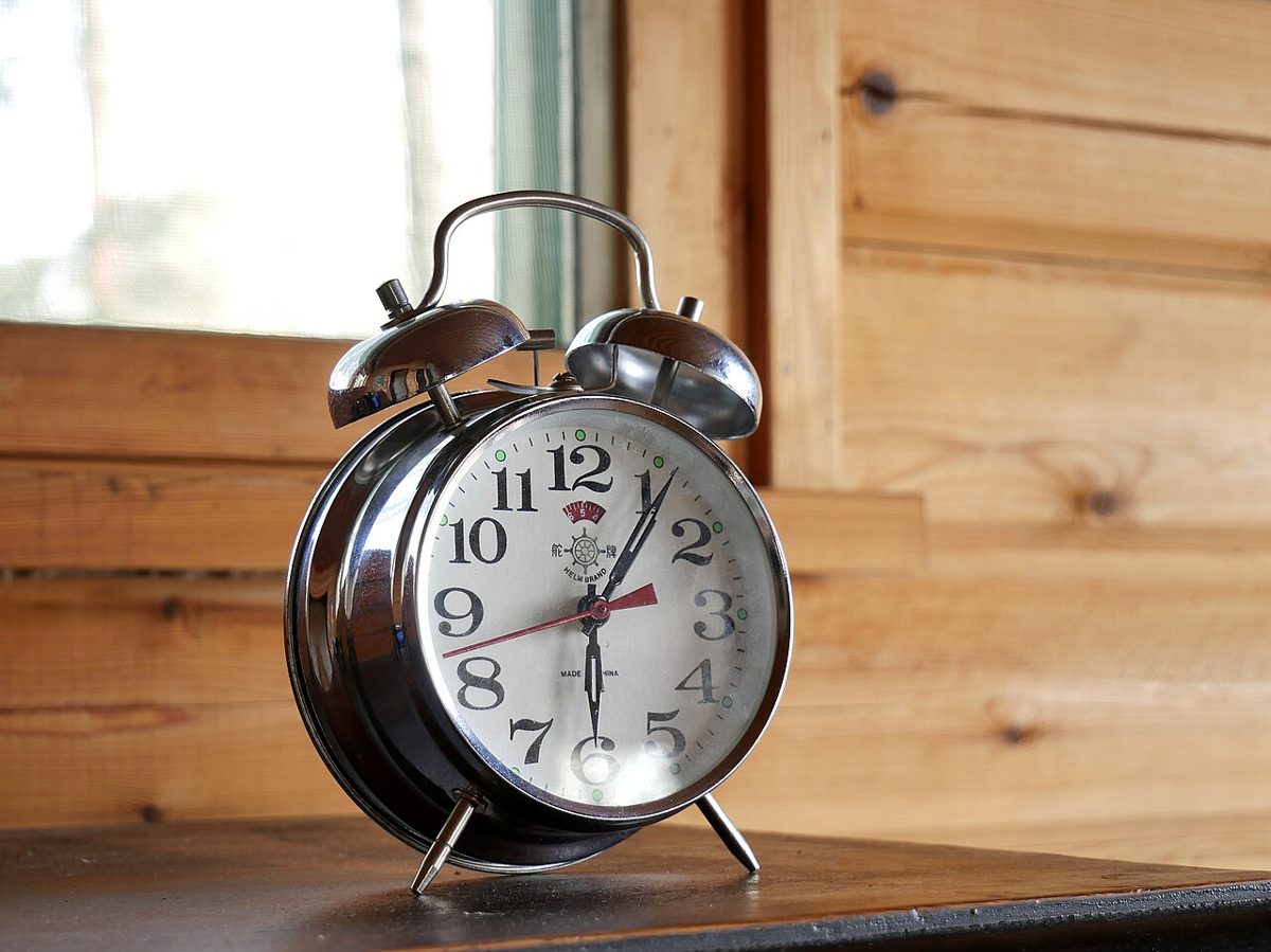 Sveglia meccanica classica vicino a una finestra, simbolo del cambio dell'ora e del sonno